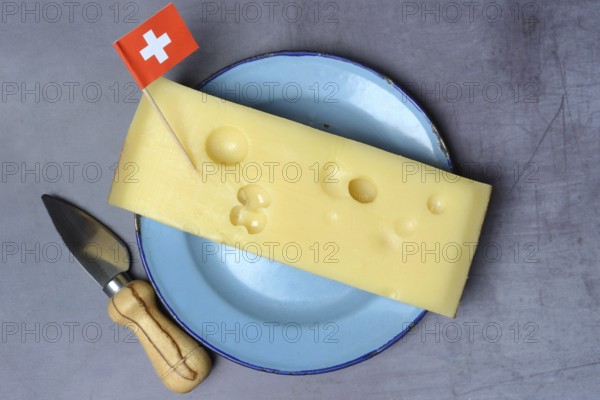 A piece of Swiss Emmental cheese on a plate and the Swiss flag
