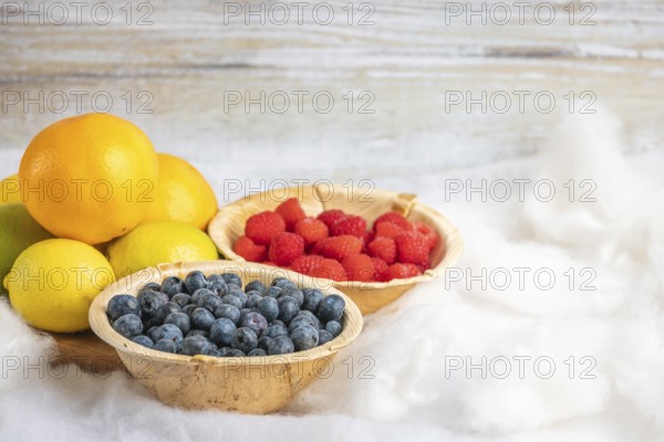 Blueberries, raspberries, oranges and lemons in wooden bowls, vitamin C, white background