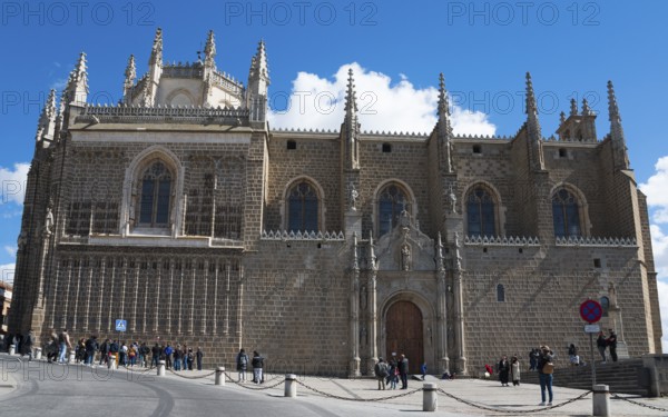 Large Gothic church with stone walls and towers under a blue sky, people standing in front of it,