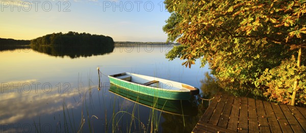 Quiet lake with jetty and rowing boat in the evening in autumn, horse chestnut with autumn leaves