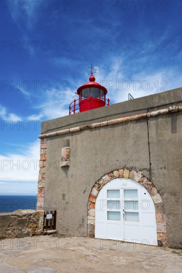Round red lighthouse on a beige building with stone accents and blue sky in the background, Fort