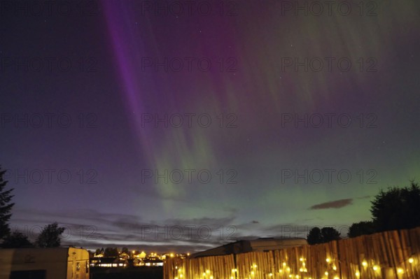 Northern Lights in the night sky above an illuminated fence and a campsite, Tönsberg, Oslofjord,