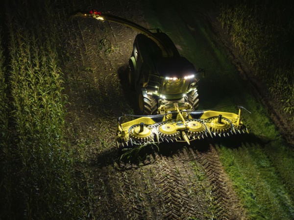 A combine harvester harvests a maize field at night, illuminated by floodlights, maize harvest,