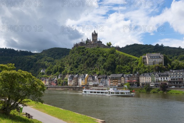 Lively town with a castle on a hill and ships on the river, surrounding green nature and clouds in