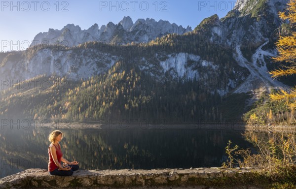 A woman doing yoga by the lake. Lotus position (Padmasana) . Vorderer Gosausee in autumn with a