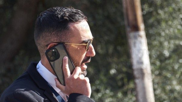Man in a suit with sunglasses talking on a smartphone outdoors, visit of Federal President