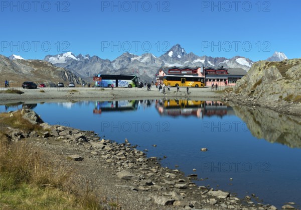 Coach with tourists and yellow bus of the Swiss PostBus AG on the Nufenen Pass, behind the mountain