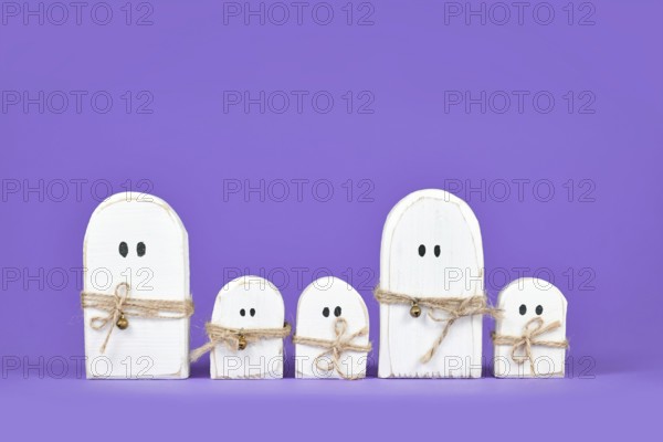 Cute wooden Halloween ghost ornaments in a row on purple background