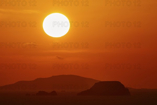 Intense sunset with a large, orange glowing sun over the ocean and islands, sunset, Kassos,