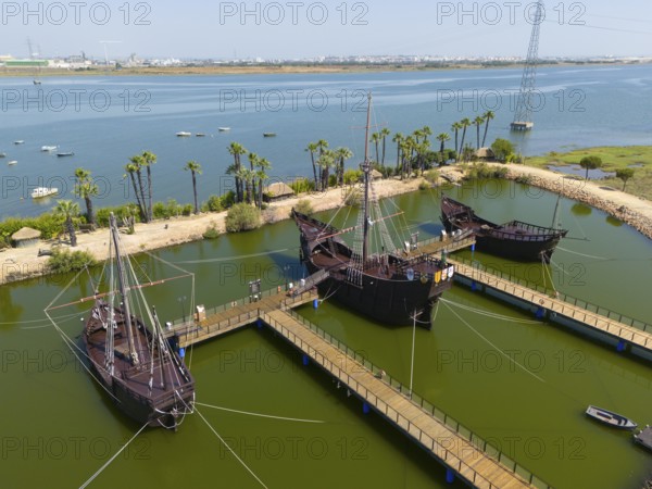 Wooden docks with replica medieval ships on the shore of a calm lake with palm trees in the