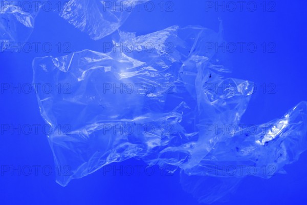 Transparent plastic bags floating underwater in blue ocean sea water, pollution by