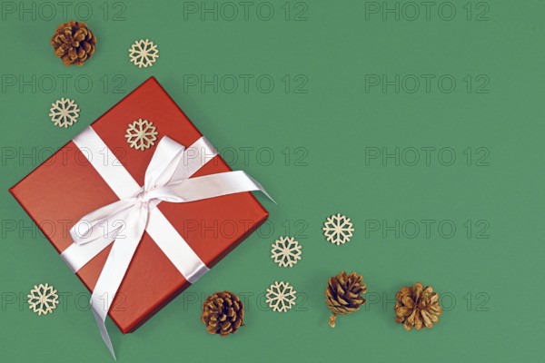Red Christmas gift box with ribbon surrounded by seasonal pine cones and wooden snowflake ornaments