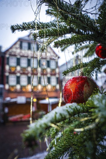 Red Christmas bauble against the snowy backdrop of a Christmas market, Black Forest, Calw, Germany,