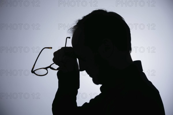 Symbolic photo on the subject of overload. Silhouette of a man rubbing his aching head. Berlin,
