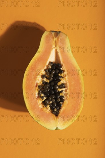 Ripe cut papaya on orange pastel background. Top view, flat lay, close up, hard light. Tropical,