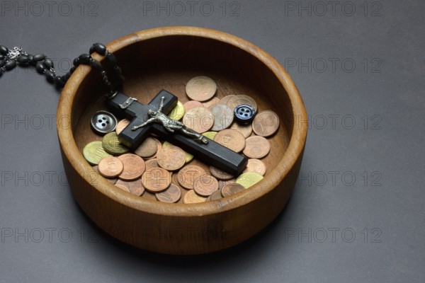 Crucifix with coins and buttons in a wooden bowl, church and money