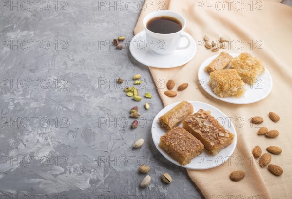 Traditional arabic sweets (basbus, kunafa, baklava) and a cup of coffee on a gray concrete