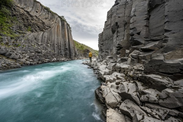 Tourist standing by the river in Stuðlagil Canyon, turquoise blue river between basalt columns,