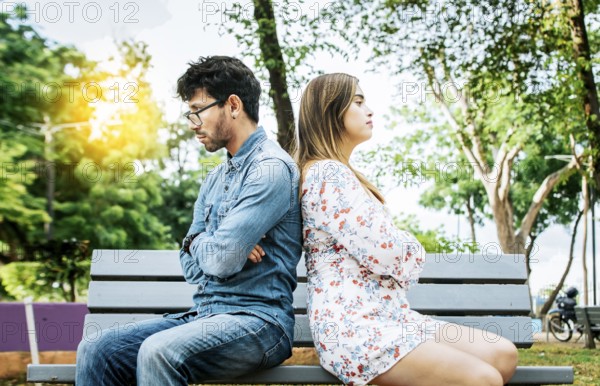 Upset young couple sitting back to back in a park, unhappy couple sitting back to back on bench.