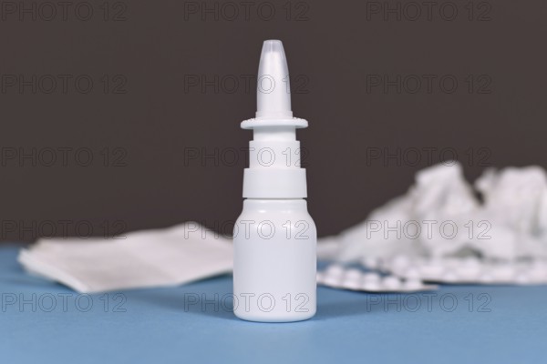Nasal spray bottle with crumbled tissues and pills used against common cold in blurry background