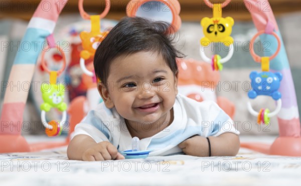 Baby boy playing and smiles lying on bed with pacifier on mouth