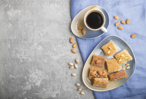Traditional arabic sweets (basbus, kunafa, baklava) and a cup of coffee on a gray concrete