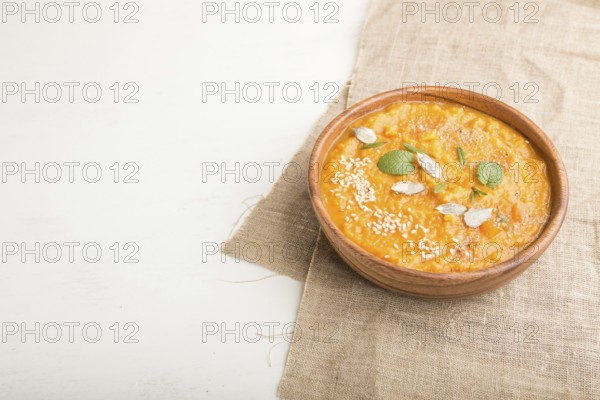 Sweet potato or batata cream soup with sesame seeds in a wooden bowl on a white wooden background