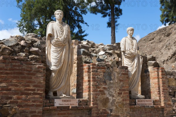 Two Roman statues made of stone, with name plaques, embedded in ancient brick structures and trees