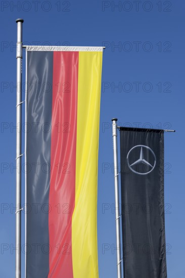 Two flags against a blue sky, one showing the German national colours, the other the Mercedes logo