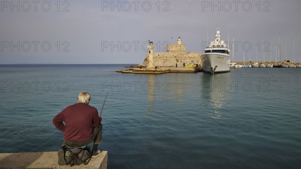 A man fishing on a shore with a view of an old fortress and a luxury yacht at sunset, Fort of Saint