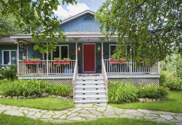 Blue and tan country cottage style residential home facade with veranda in summer, Quebec, Canada,