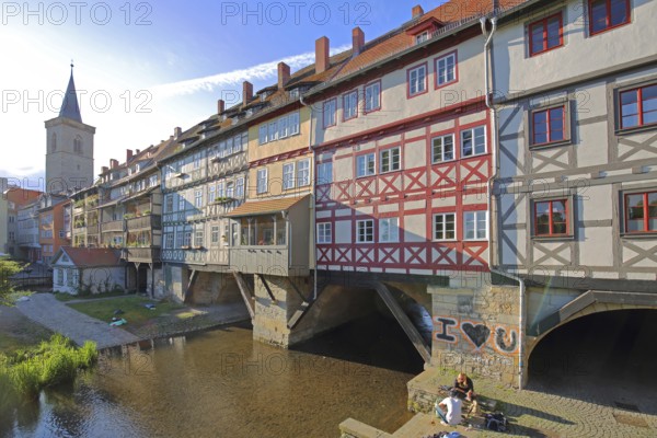 Famous Krämerbrücke and Gothic Ägidienkirche with river Gera and people sitting on the bank, idyll,