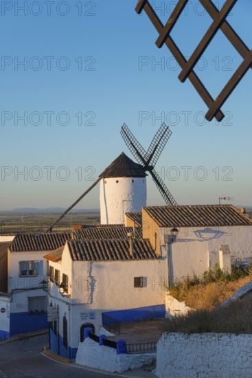 Windmill in front of white houses at sunset in a rustic village with warm light and blue accents