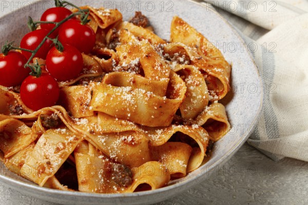Pappardelle pasta with bolognese sauce, topped with parmesan cheese and cherry branch, homemade, no