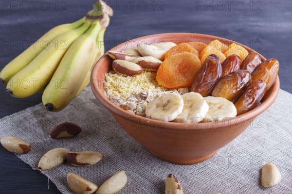A plate with muesli, banana, dried apricots, dates, Brazil nuts on a black wooden background. close