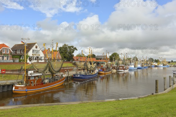 View of historic houses with colourful facades at the old harbour of Greetsiel, with fishing boat,