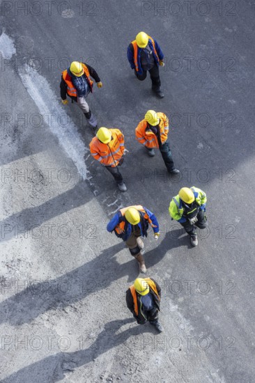 Several construction workers wearing hard hats walk over tarmac. They cast long shadows. Stuttgart,