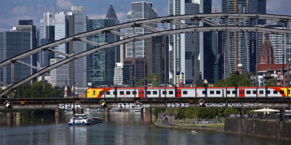 Main with regional railway on the Deutschherrnbrücke and a cargo ship in front of the skyline of