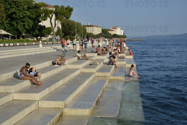 Visitors basking in the evening sun at the Sea Organ by architect Nikola Bašic, Zadar, Dalmatia,