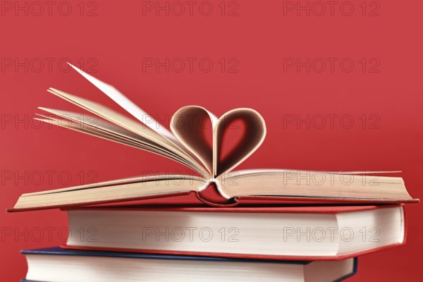 Pages folded into heart shape on stack of old hardcover books on red background