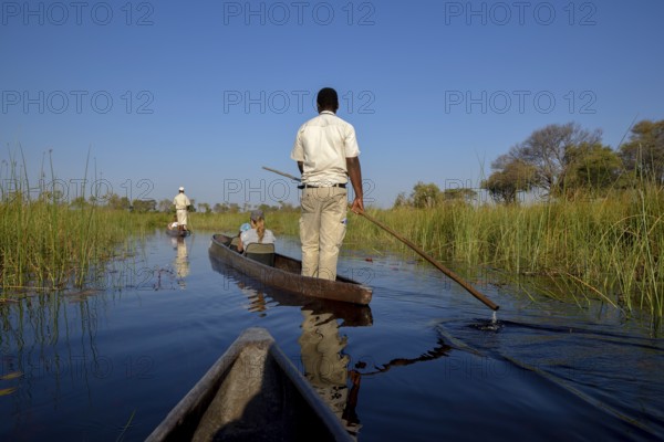 Tourists in a mokoro or dugout boat on safari in swamp area, Gomoti Plains Camp, Gomoti Concession