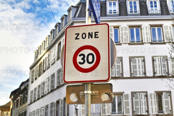 Square shaped 30km/h speed limit zone sign in front residential buildings in background