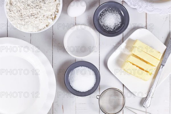Pie crust ingredients in bowls. Flour, sugar, salt, ice water, butter and egg on wooden table