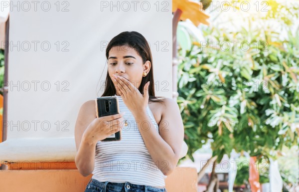 Girl with cell phone with a surprised face leaning on a wall. Young woman with the cell phone with