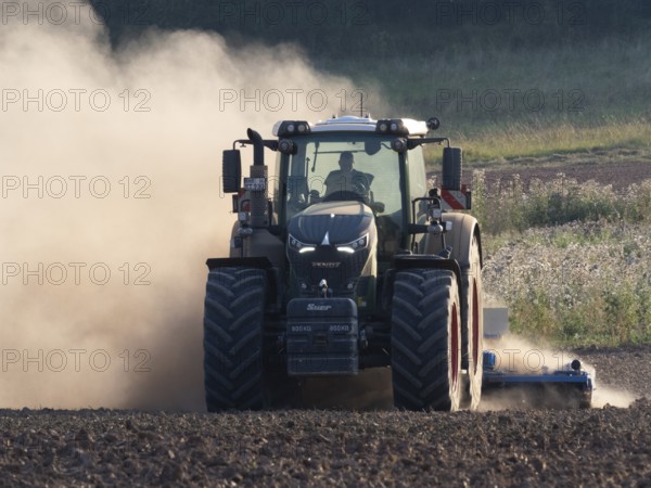 Agricultural tractor, cultivating a field, after the corn harvest, surrounded by dust due to very