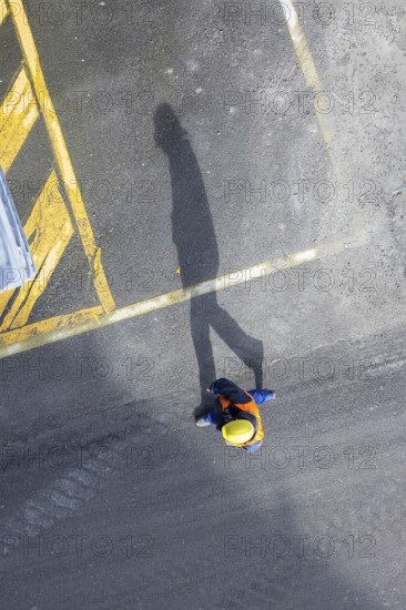 A construction worker in a hard hat walks over tarmac. He casts a long shadow. Stuttgart,
