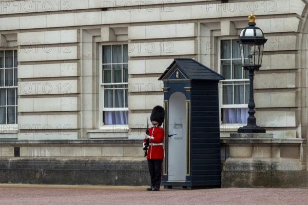 A guard in red uniform stands in front of a sentry box next to a lantern at Buckingham Palace,