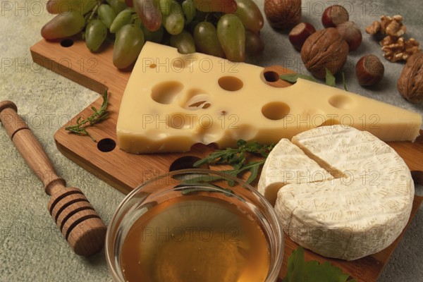 Cheese with big holes, emmental, maasdam, brie cheese, on a cutting board, with grapes and honey,
