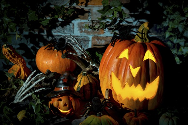 Halloween pumpkin surrounded by spiders, decorative pumpkins and bone hands in a gloomy setting