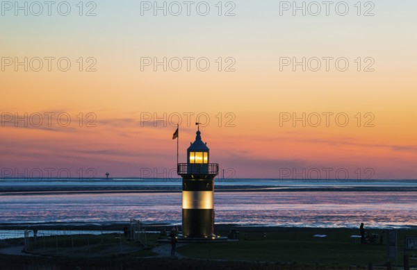 Black and white lighthouse, called 'Kleiner Preuße', lighthouse and boat at sunset on the coast,